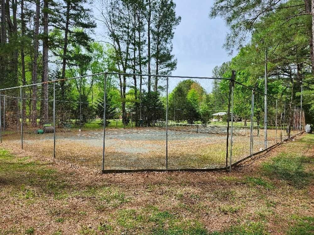 A baseball field with a fence in the middle of a park surrounded by trees.