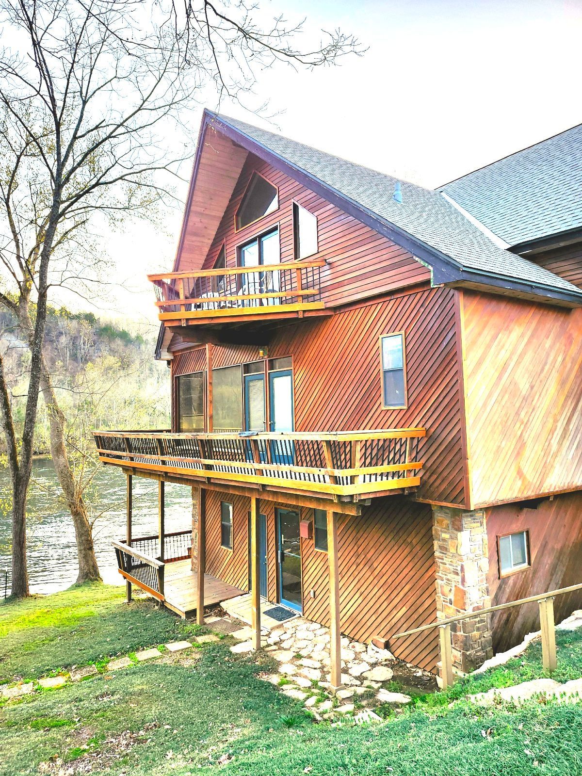 A large wooden house with a large deck overlooking a river.