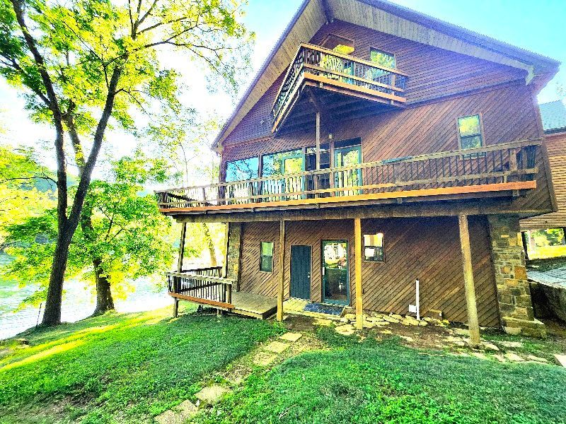 A large wooden house with a large deck overlooking a lake.