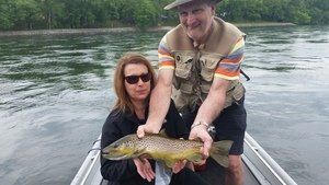 A man and a woman are holding a brown trout in a boat.
