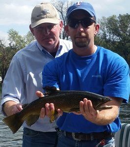 A man in a blue columbia shirt is holding a fish