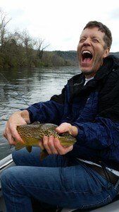 A man is sitting in a boat holding a brown trout.