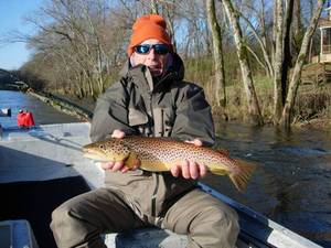 A man is sitting in a boat holding a brown trout.