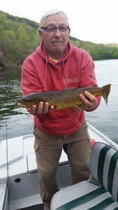 A man is holding a brown trout in his hands while sitting on a boat.