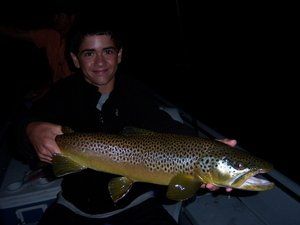 A young man is holding a large brown fish in his hands