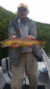 A man is standing on a boat holding a large brown trout.
