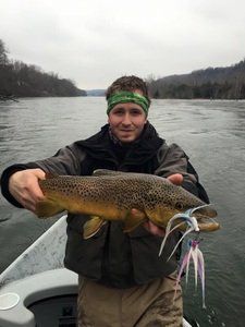 A man in a boat is holding a brown trout in his hands.