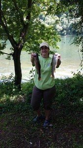 A woman is holding two fish in her hands in front of a lake.
