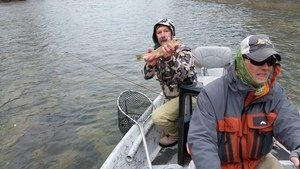 Two men are fishing in a boat and one of them is holding a fish.