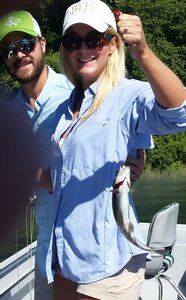 A woman is holding a small fish next to a man on a boat.