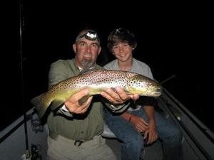 A man and a boy are sitting in a boat holding a brown trout.