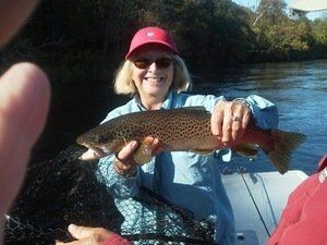 A woman in a red hat is holding a brown trout