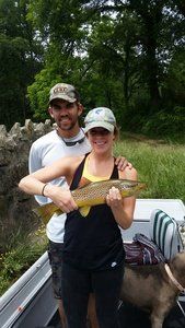 A man and a woman are standing in a boat holding a fish.