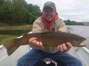 A man is sitting on a boat holding a brown trout.