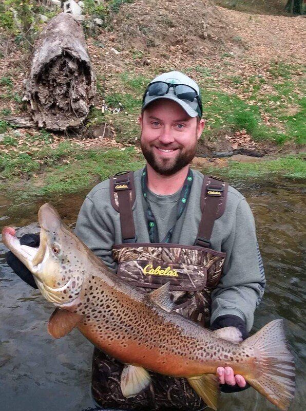 A man is holding a large brown trout in his hands.