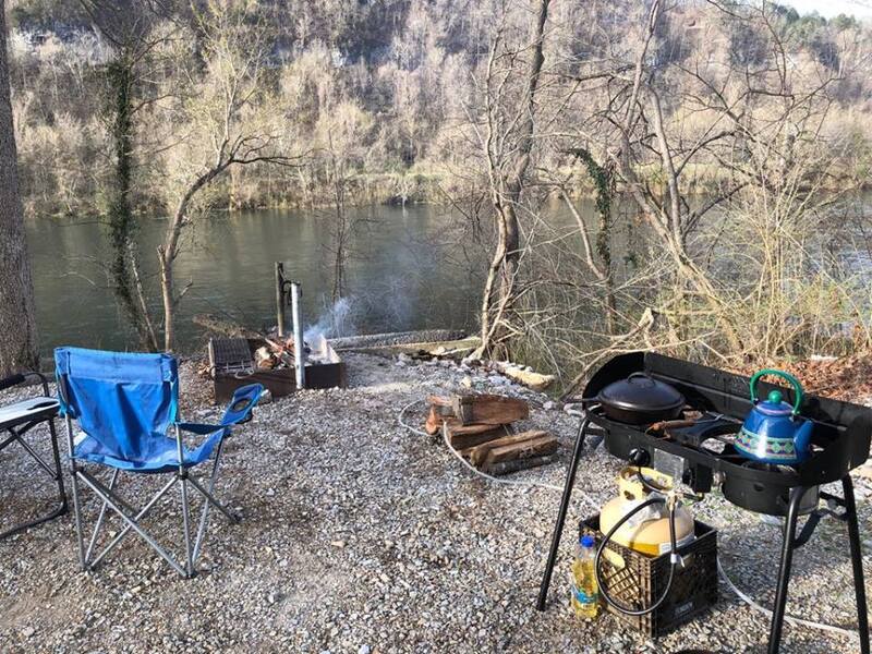 A campsite with a fire pit , chairs , a stove and a kettle.