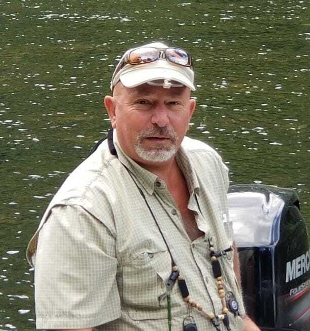 A man wearing a hat and sunglasses is standing next to a mercury outboard motor