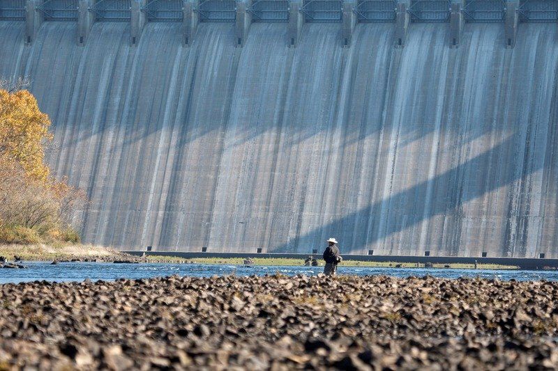 A man is fishing in front of a large dam.