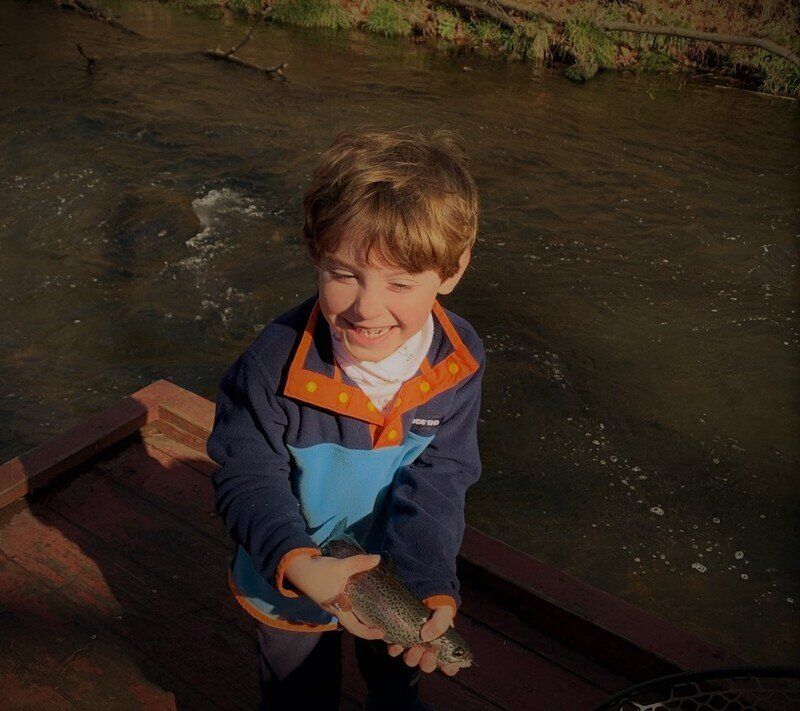 A young boy in a blue and orange jacket is holding a fish
