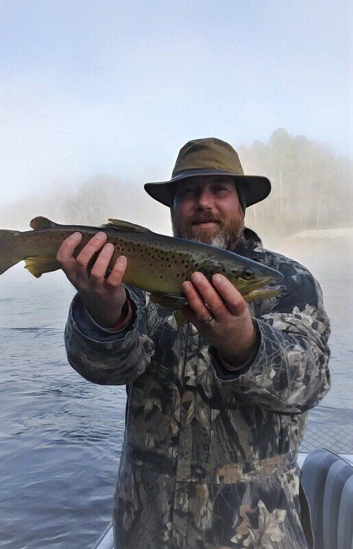 A man in a hat is holding a brown trout in his hands.