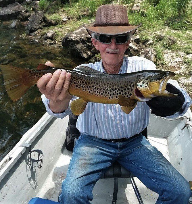 A man in a boat is holding a brown trout