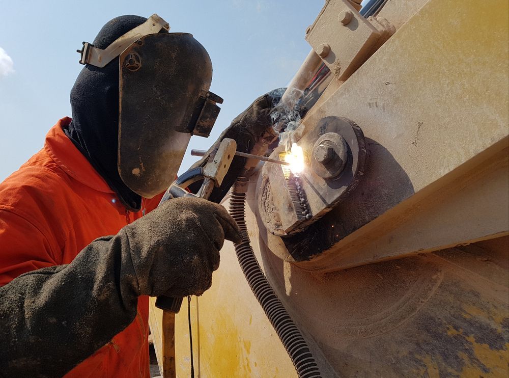 Welder in Orange Suit and Mask Welding Metal Outdoors, Bright Sparks, Close-up — Cairns Metal Works in Portsmith, QLD