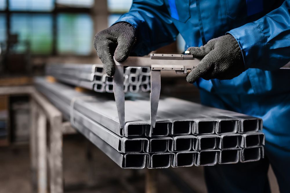 Person in Blue Overalls Measuring Metal Beams With a Caliper in a Workshop — Cairns Metal Works in Portsmith, QLD