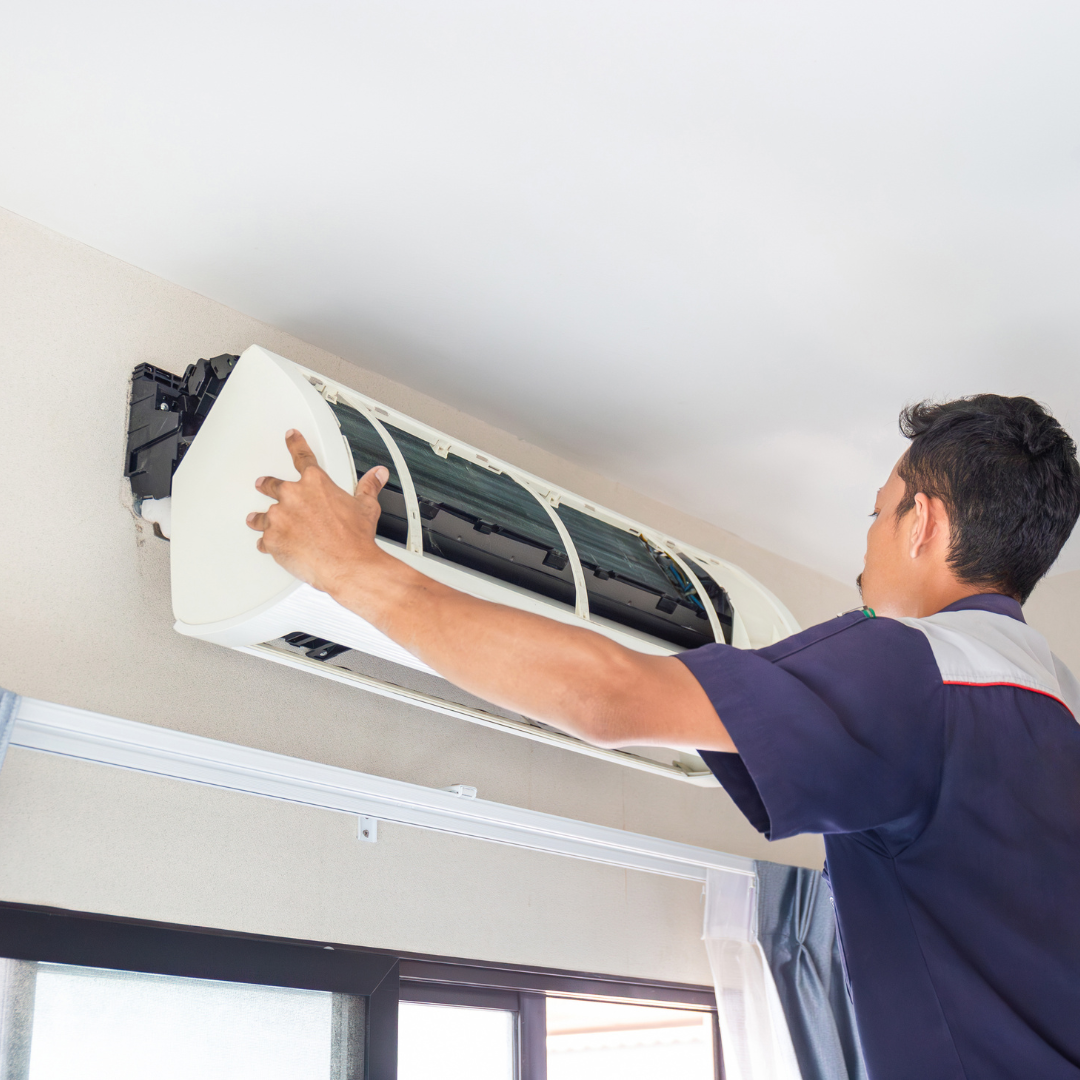 Man in blue shirt installing an AC unit on a white wall.