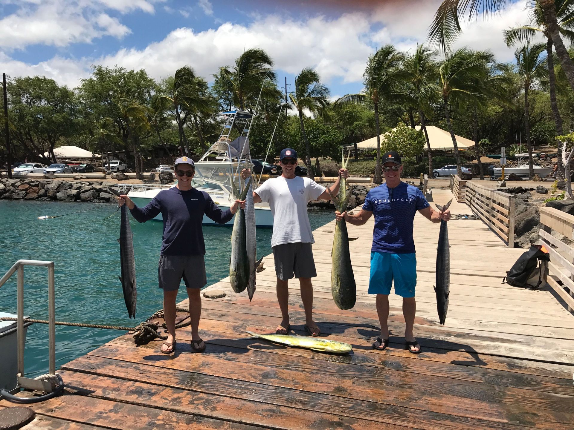 Three men are standing on a dock holding fish.