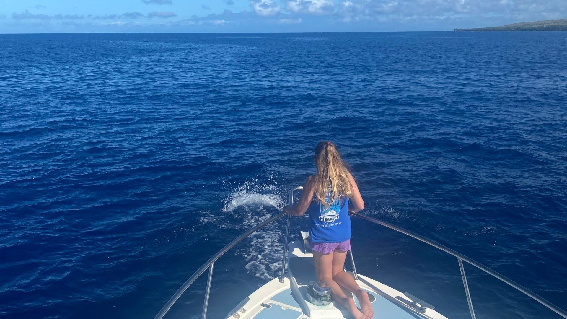 A young girl is standing on the bow of a boat in the ocean.