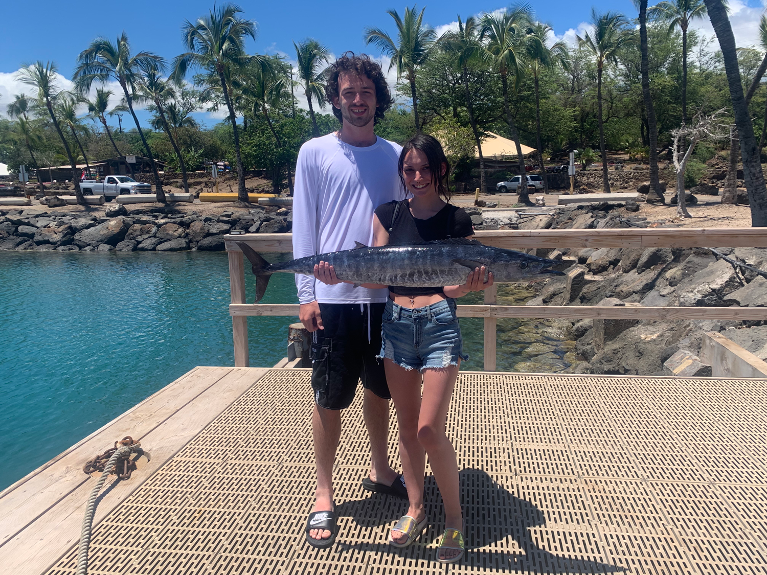 A man and a woman are standing on a dock holding a large fish.