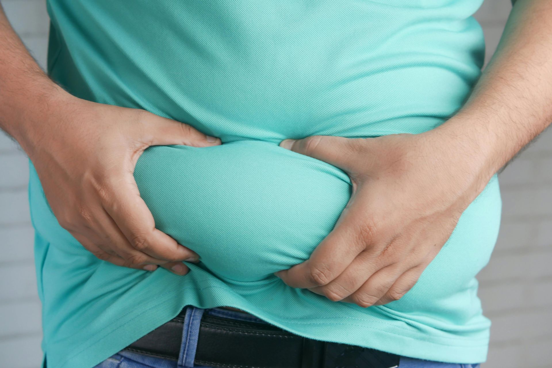 A man in a green shirt is holding his belly with his hands.