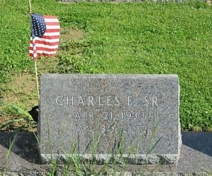 Gravestone marked “CHARLES E. SR” with an American flag in a grassy cemetery plot