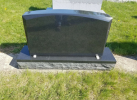 Black polished gravestone on a concrete base in a grassy cemetery.