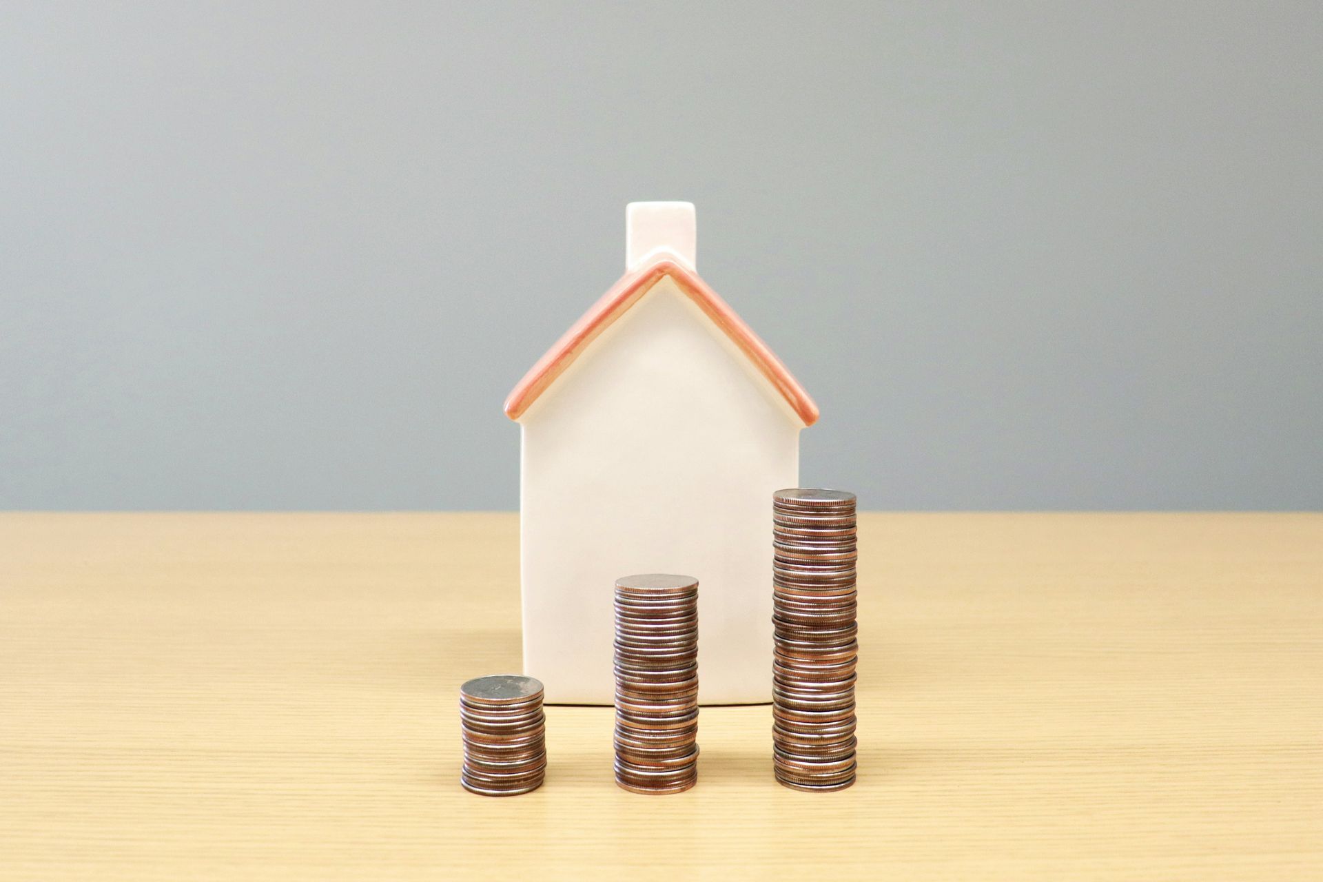 Toy house with three stacks of coins, suggesting increasing home value.