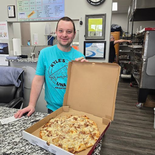 A man in a blue shirt is holding a pizza in a box.