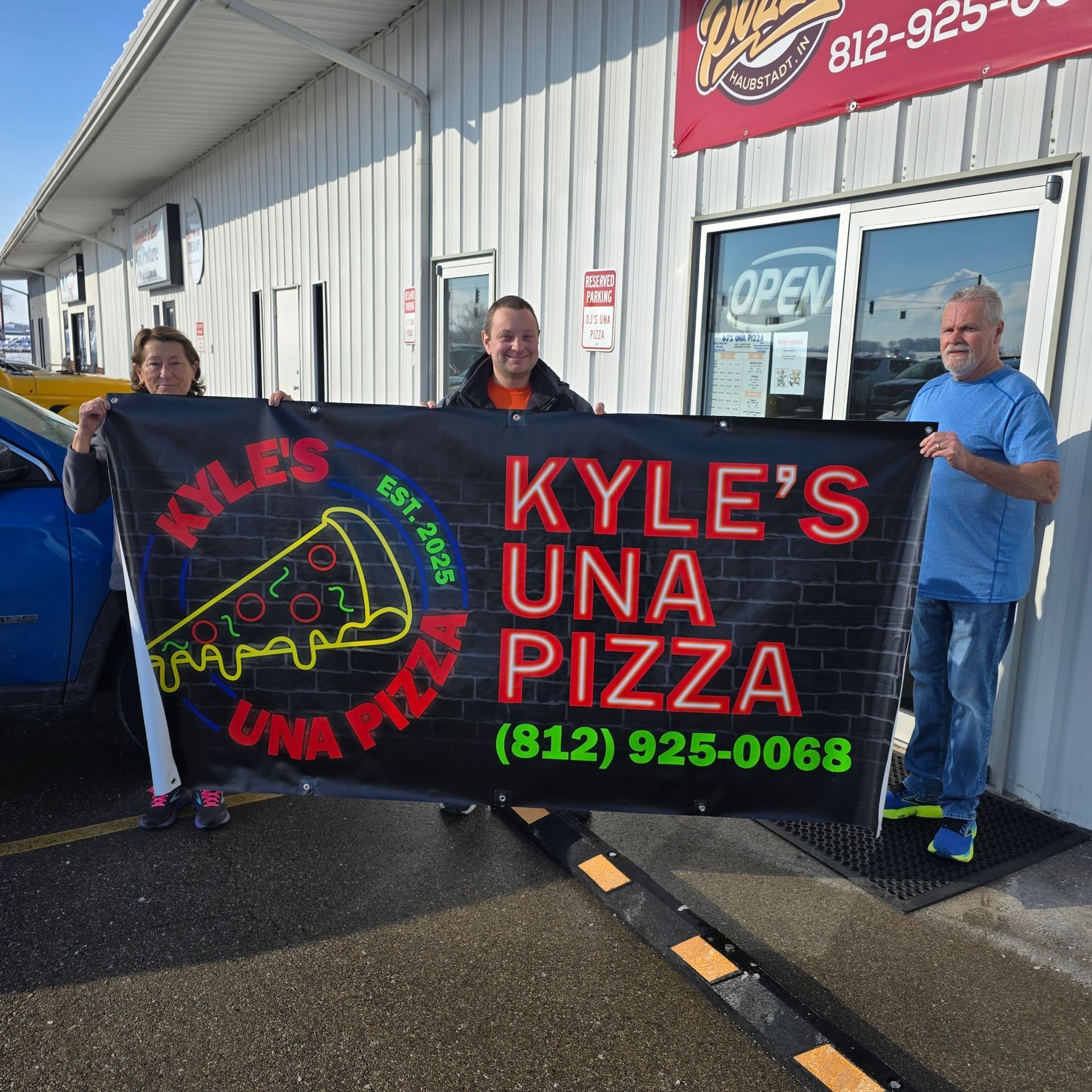 A group of people holding a kyle 's una pizza banner