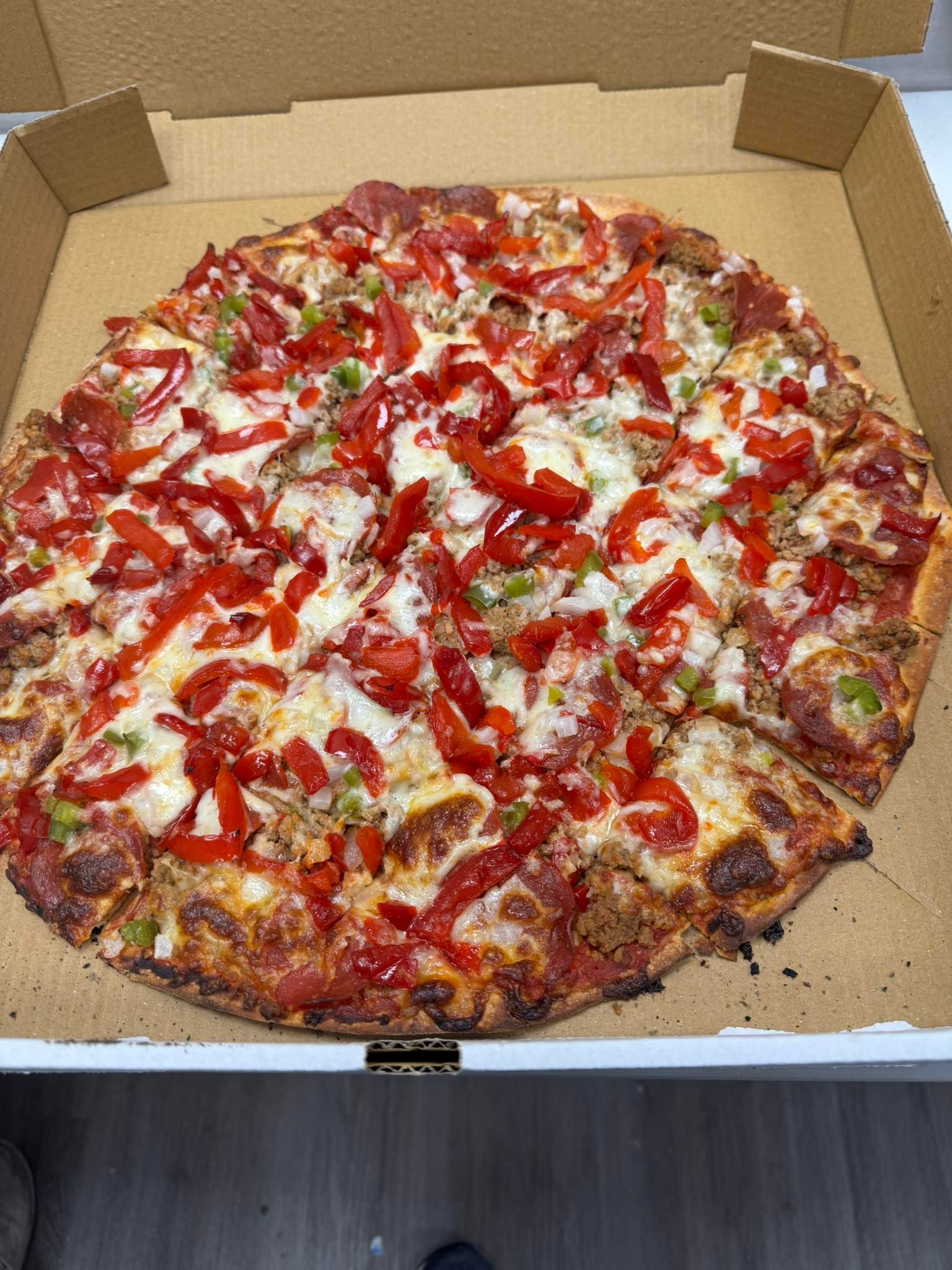 A pizza with pepperoni, cheese and peppers is in a cardboard box.