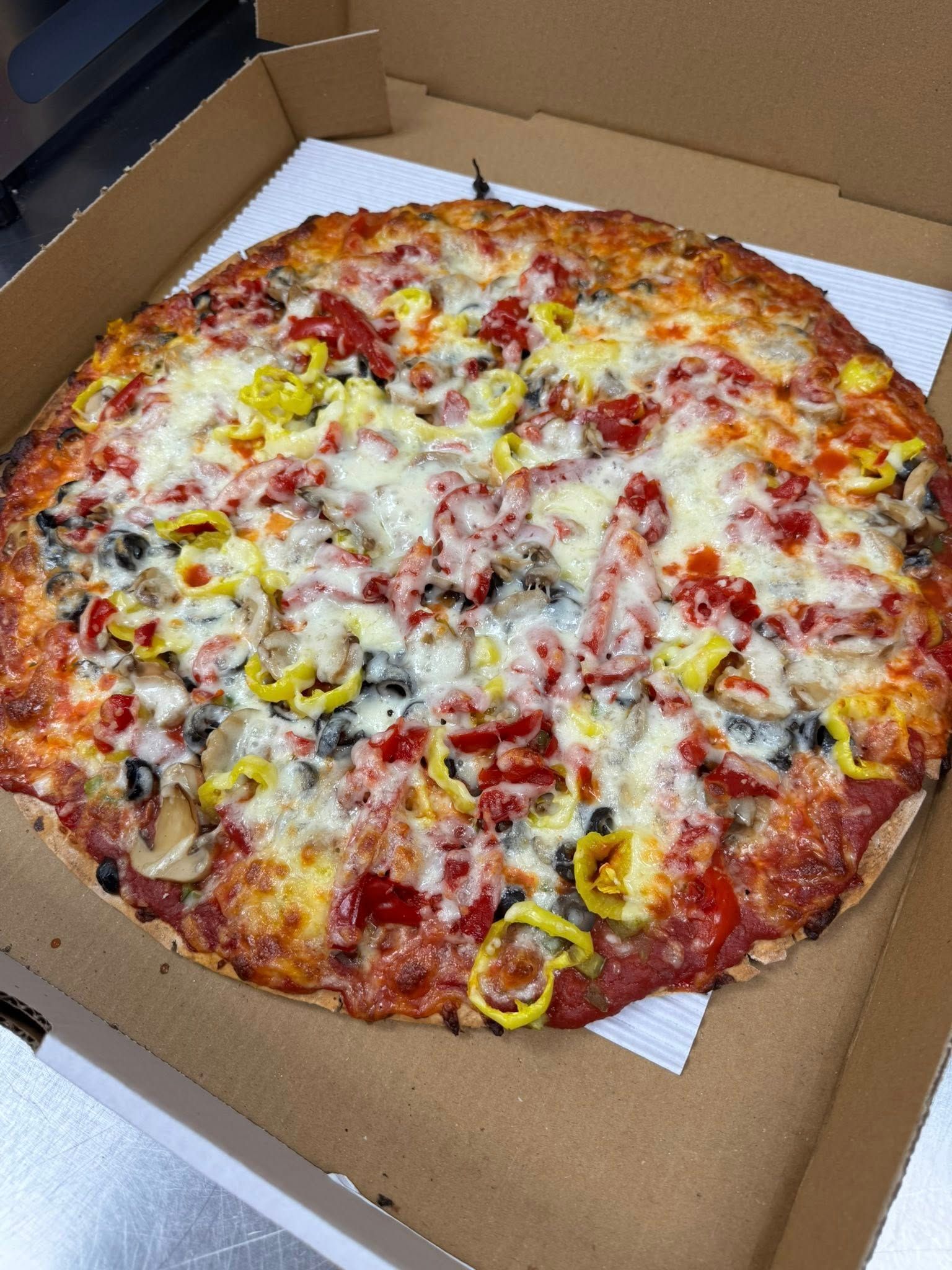 A supreme pizza is sitting in a cardboard box on a table.