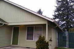 A small house with a porch and a fence in front of it.