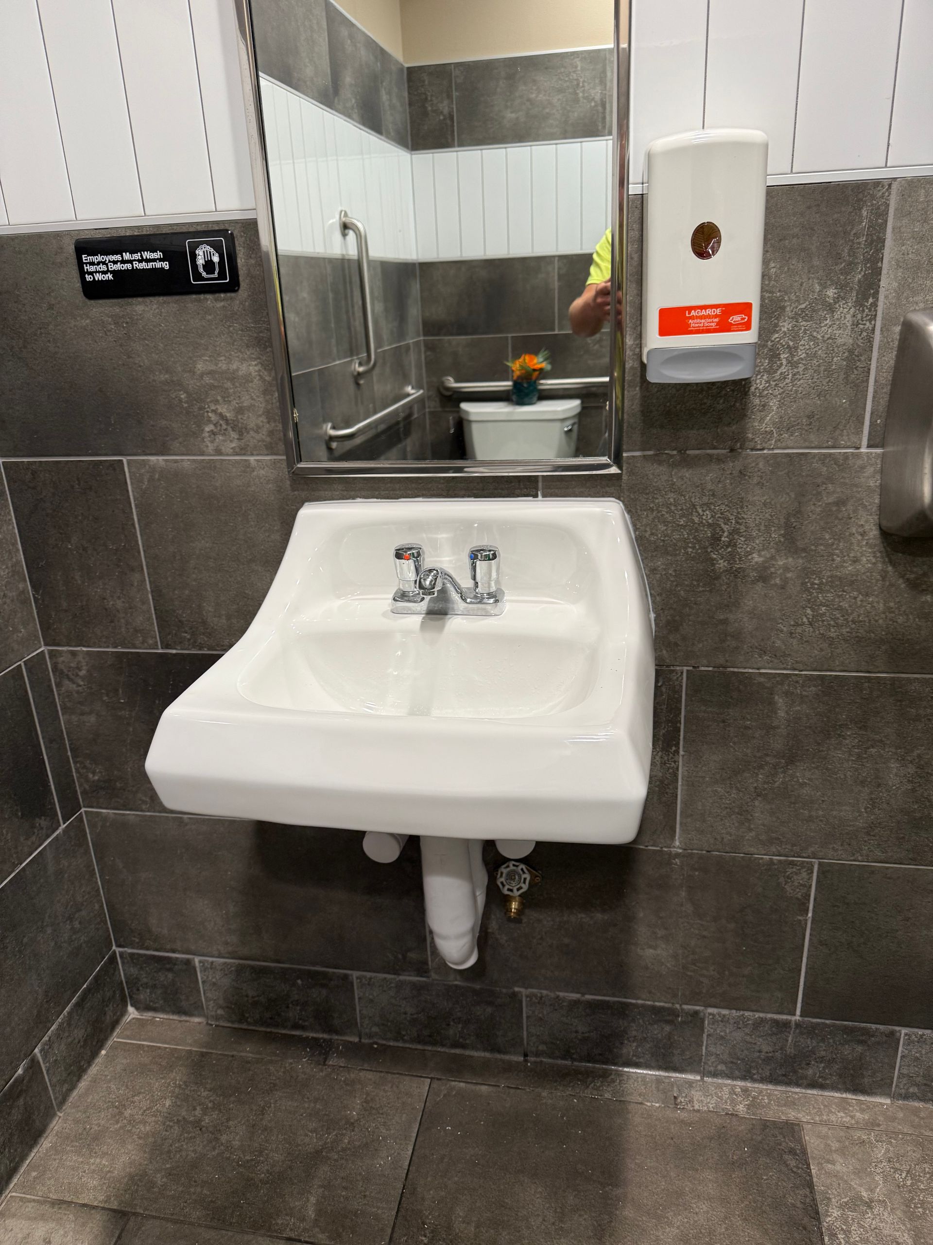 Bathroom sink with mirror, soap dispenser, and tile walls.