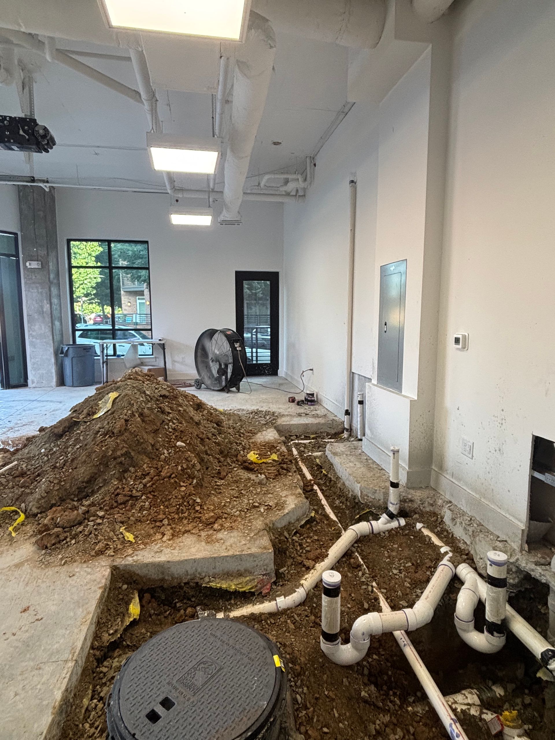 Interior construction site with exposed plumbing and dirt pile; white walls, concrete floor.