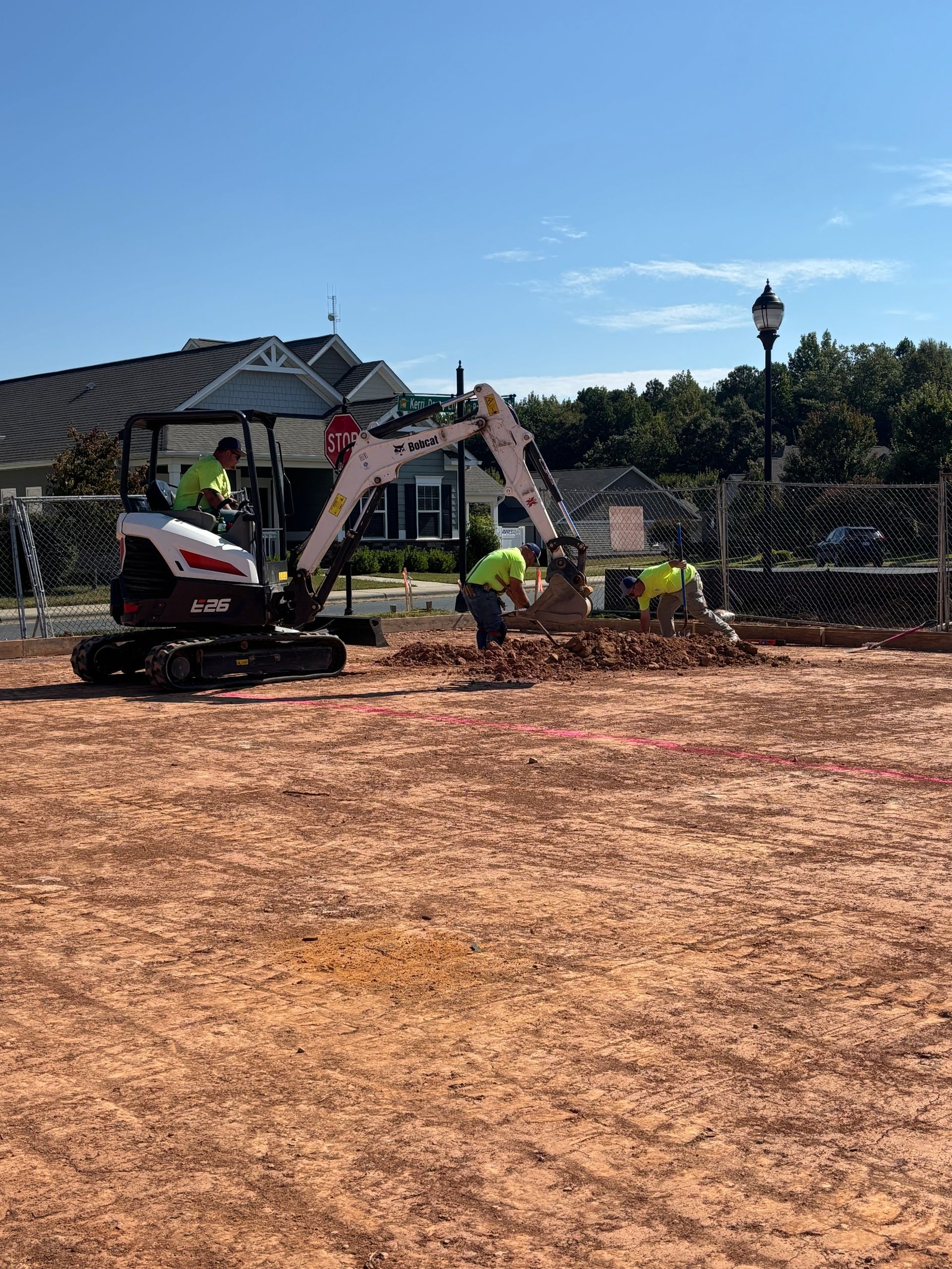 Construction site: Excavator and workers digging in dirt under a sunny sky.