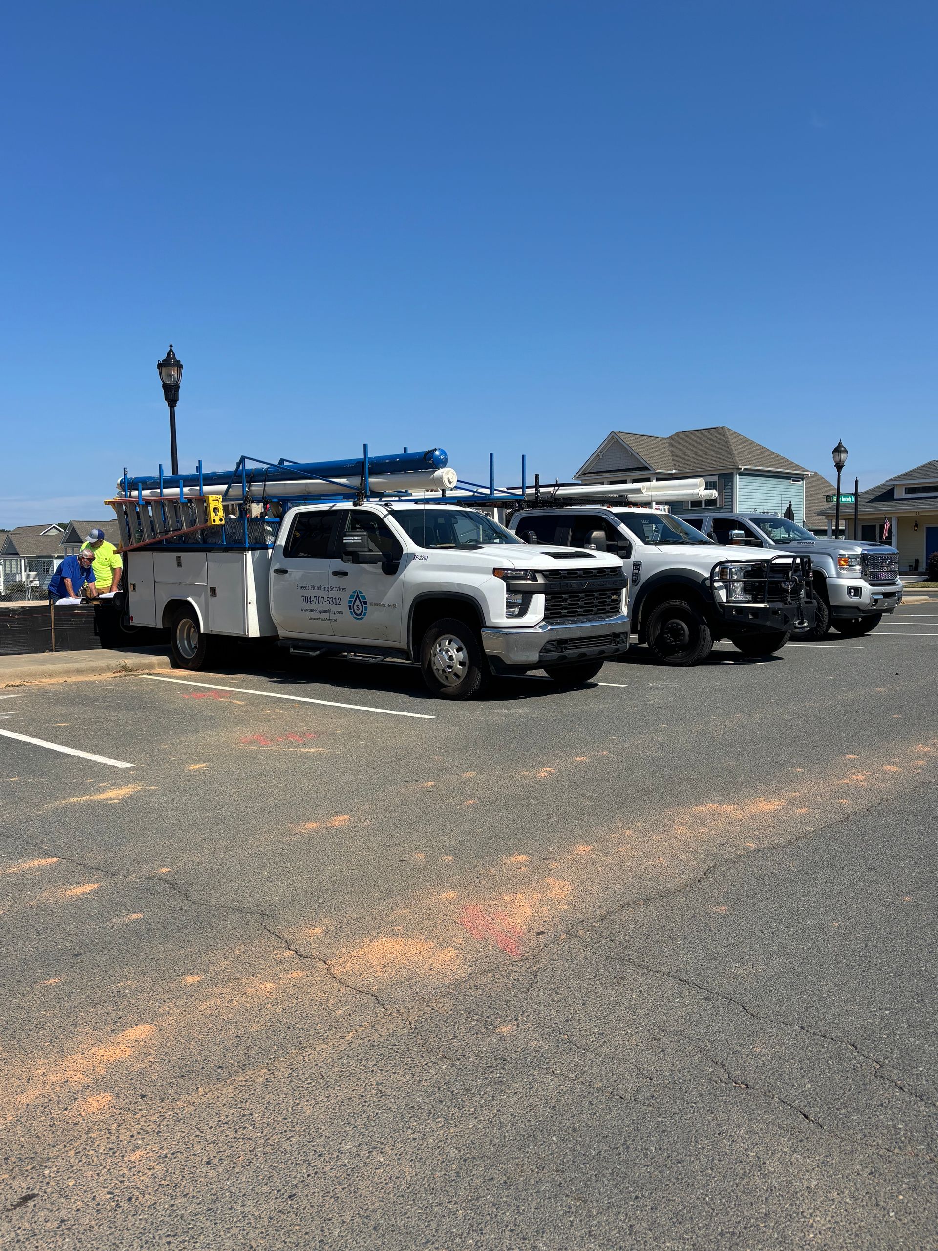Four white work trucks parked on a gravel lot under a clear blue sky.