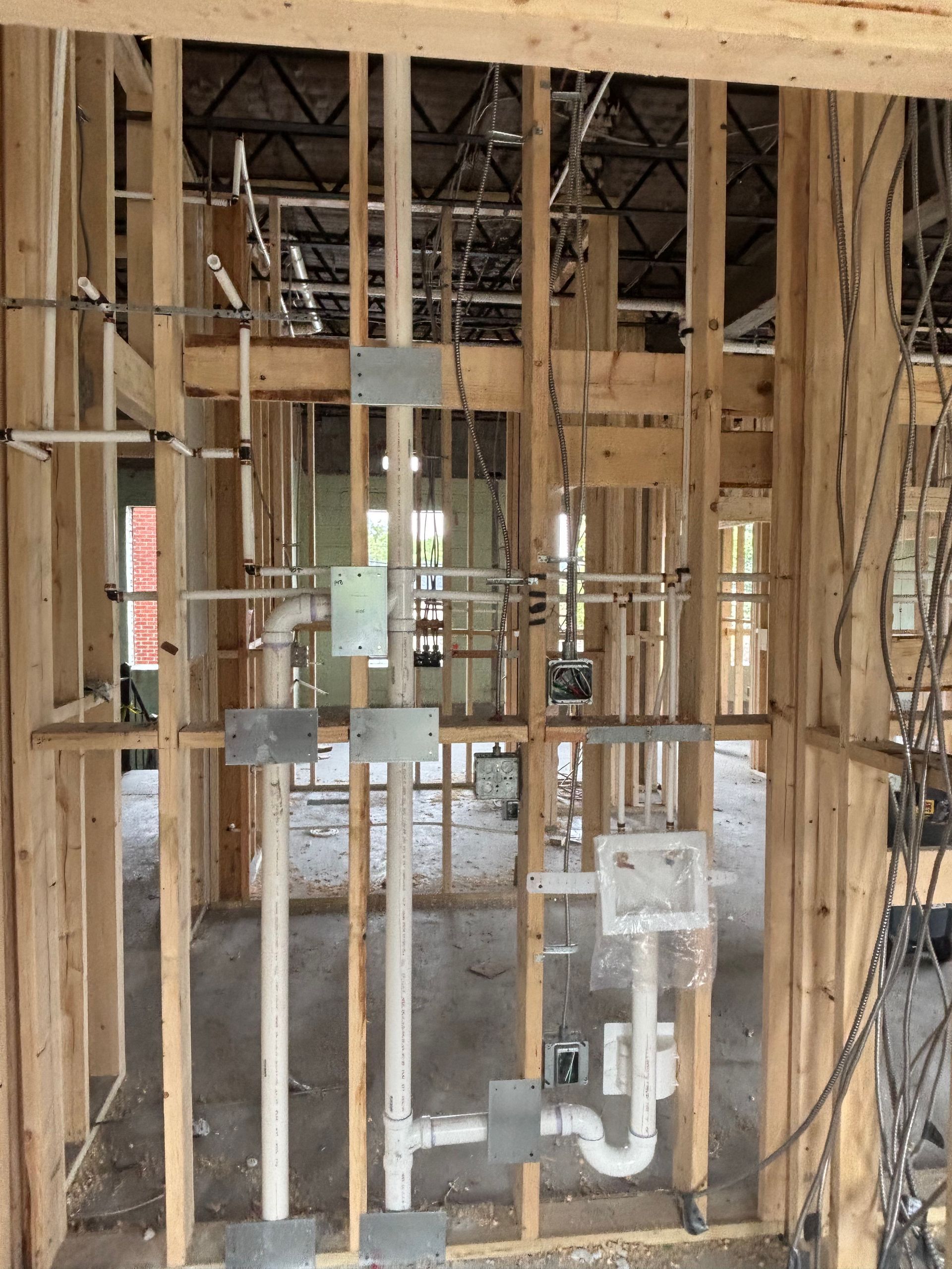 Interior view of a building under construction, showing wooden framing, plumbing, and electrical wiring.