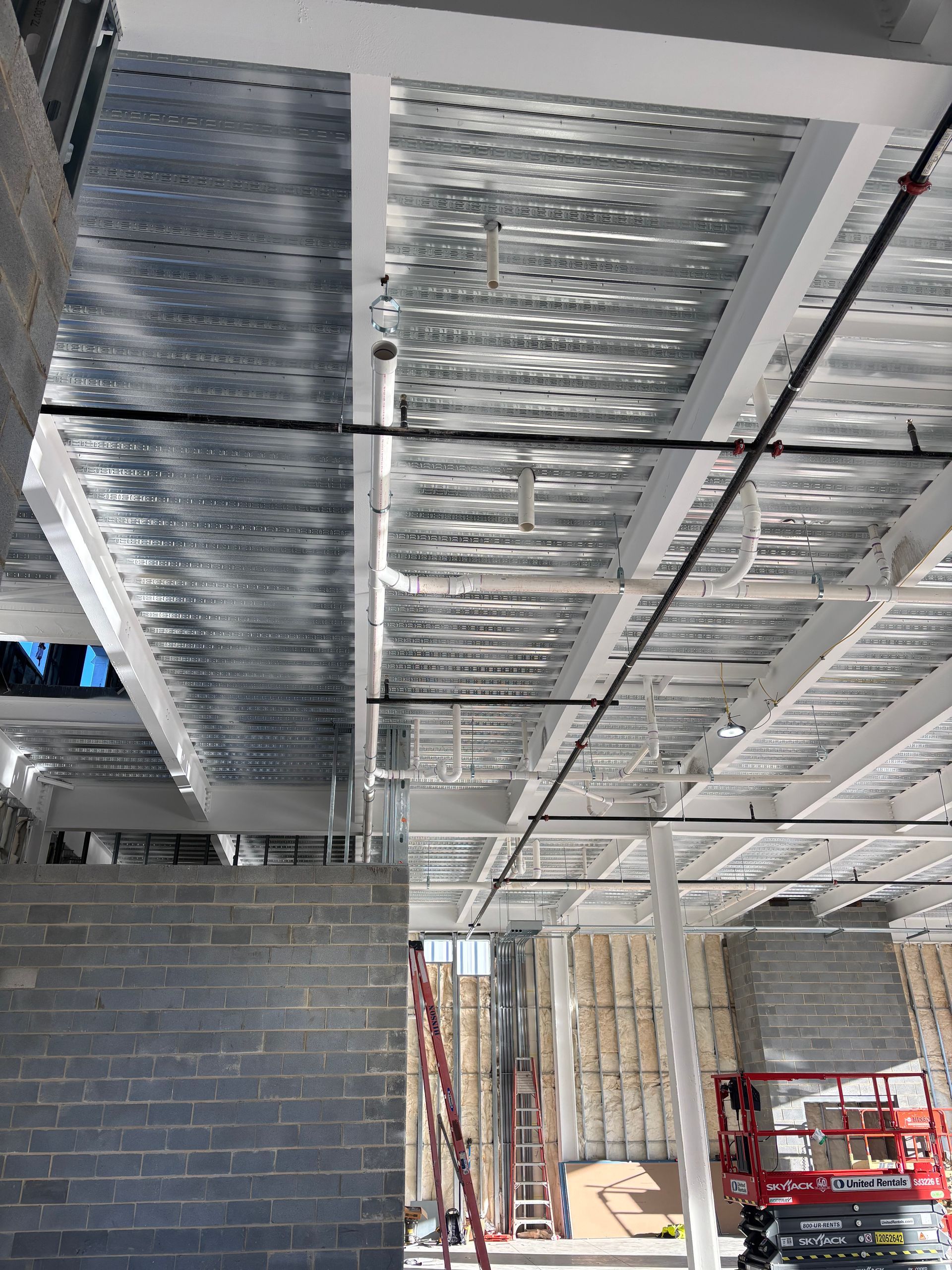 Construction site interior. Exposed metal decking ceiling, cinder block walls, and utility pipes.