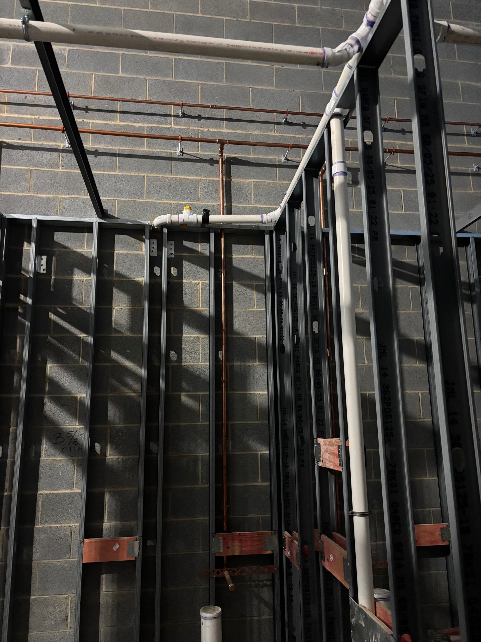 Construction site with exposed plumbing and metal framing against a gray brick wall.