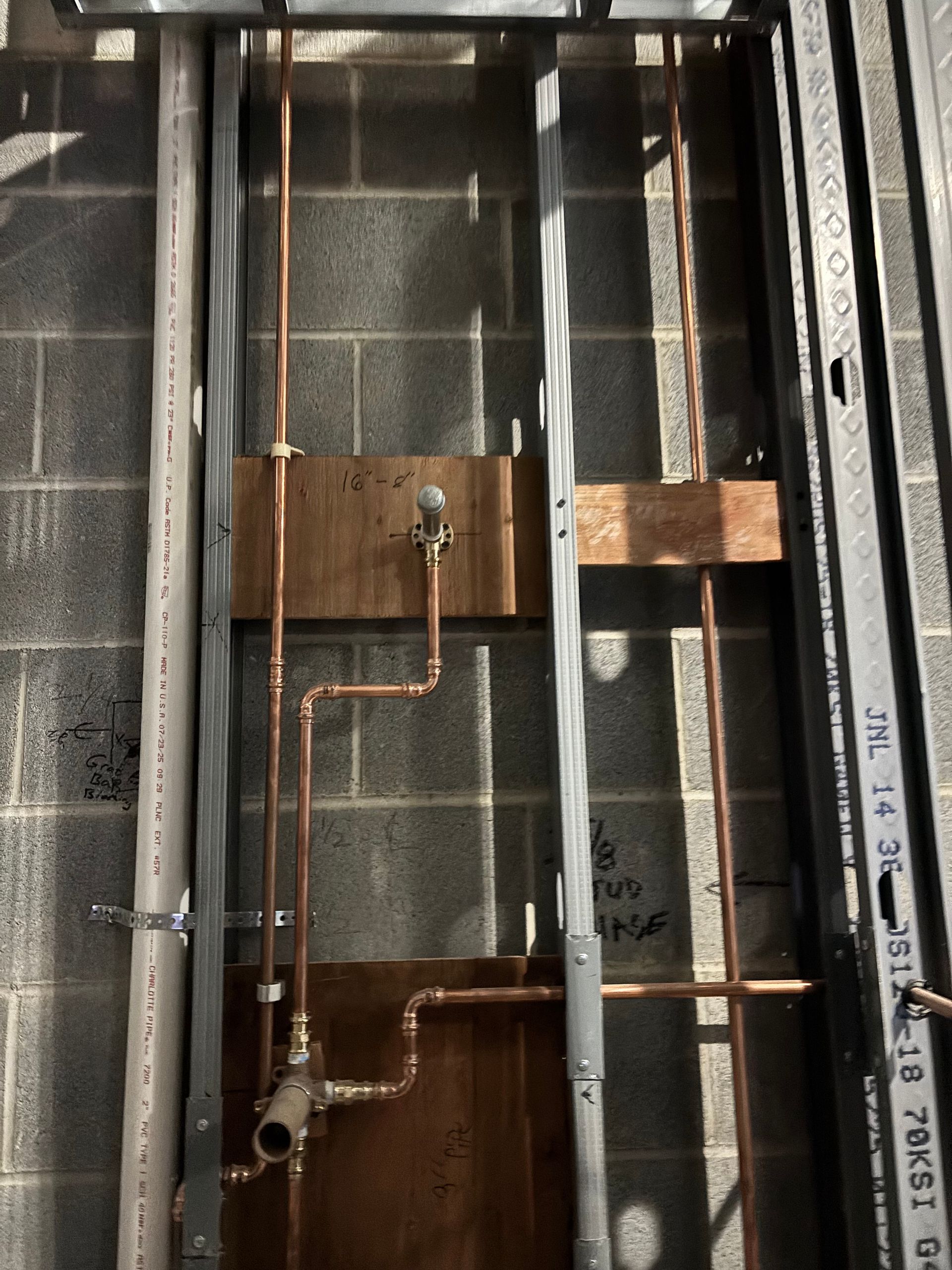 Copper pipes installed within metal framing against a concrete block wall, plumbing in progress.