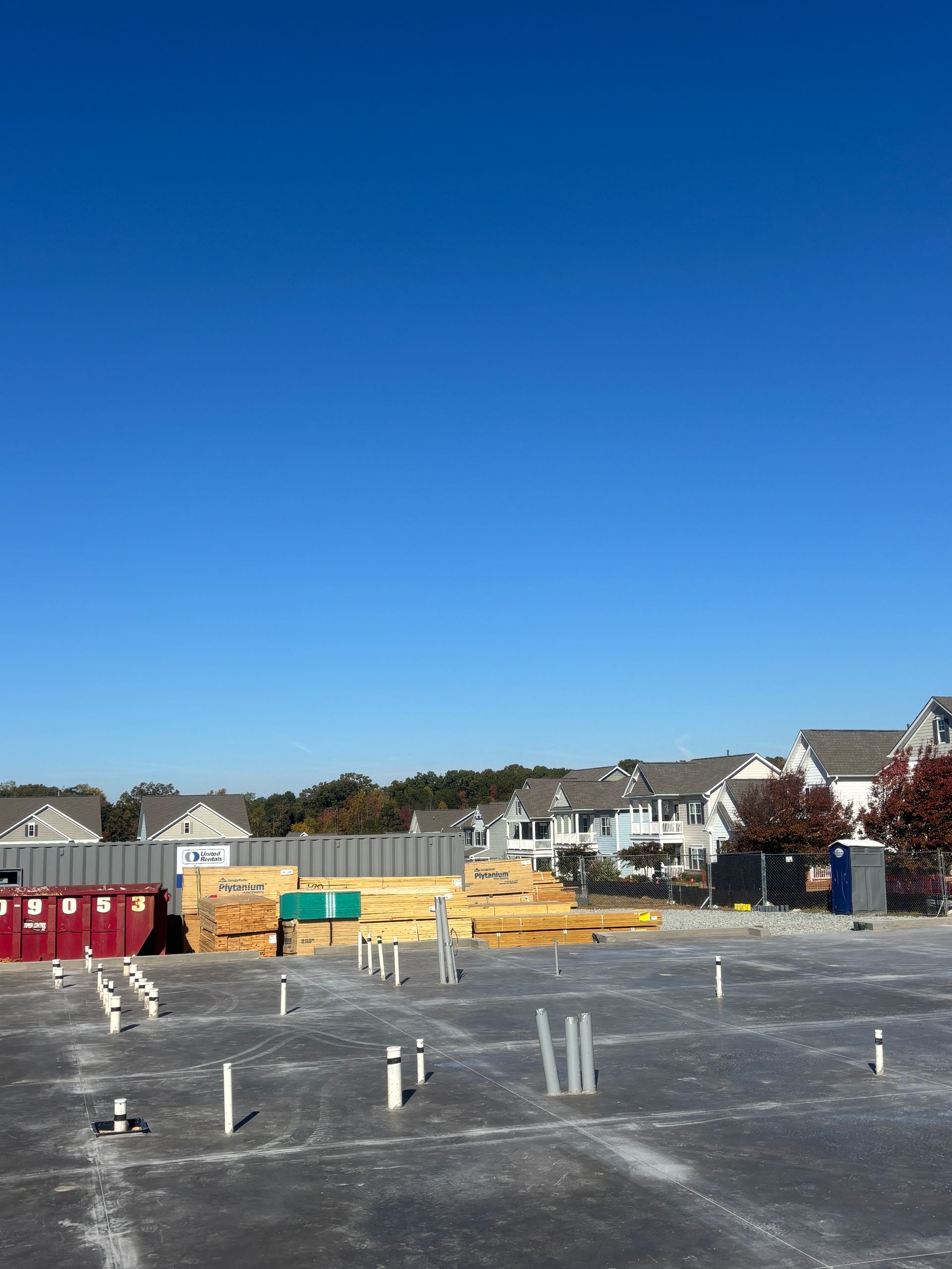 Construction site with lumber and pipes, background houses under blue sky.