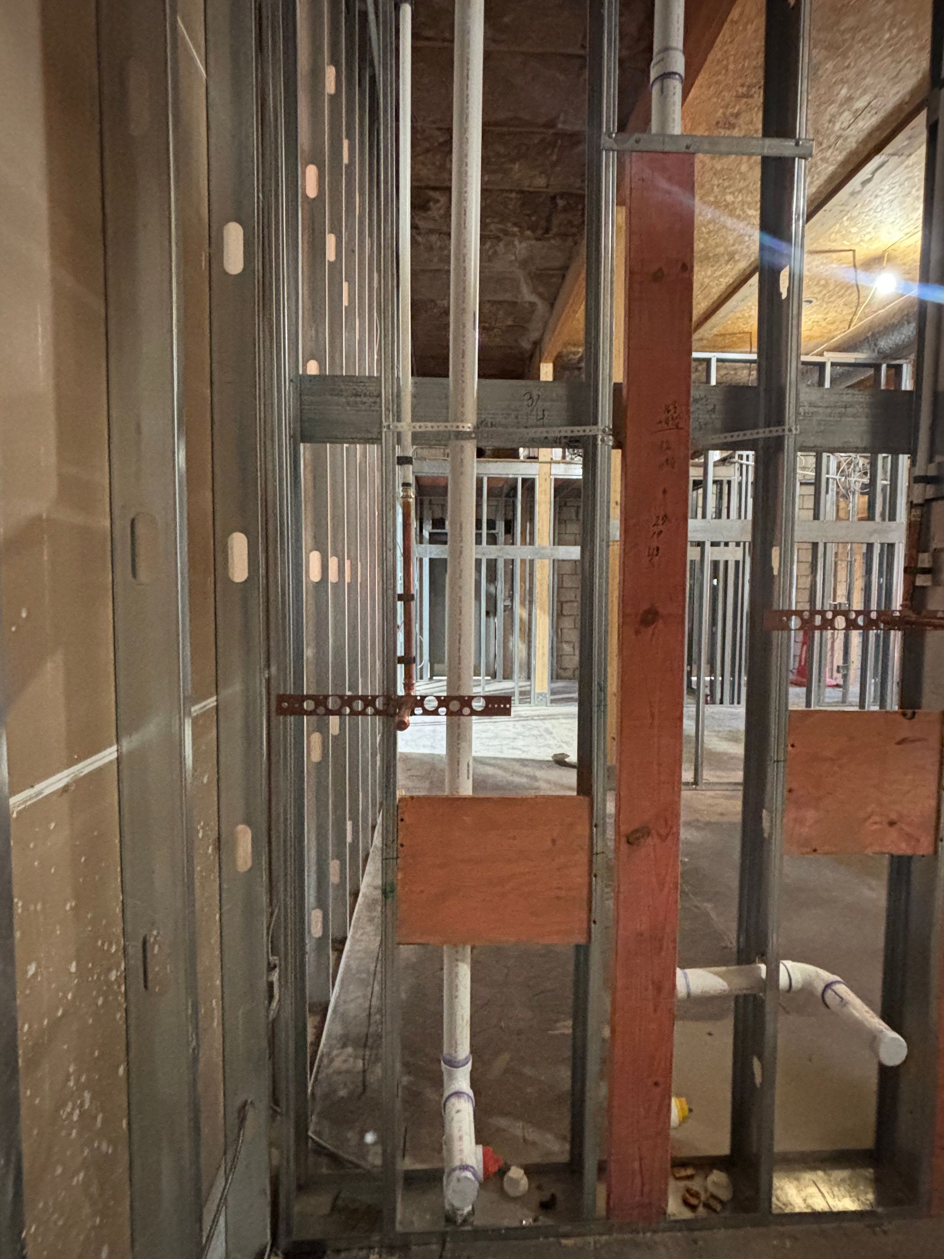 Interior of a building under construction. Metal studs, pipes, and wood framing are visible.